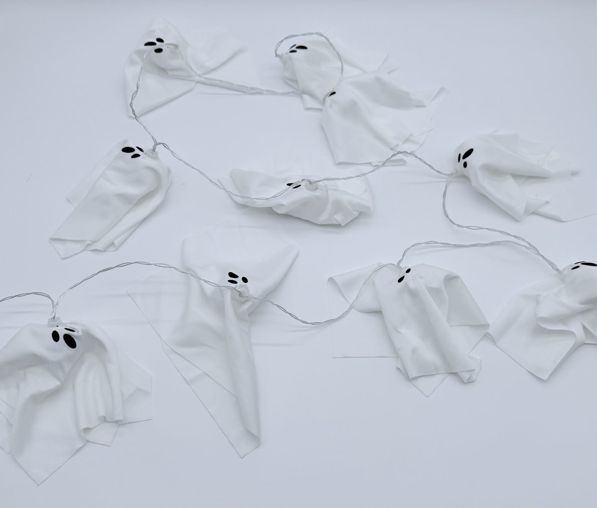 White ghost garland with black embroidered eyes and mouths, strung along a thin wire against a plain white background.
